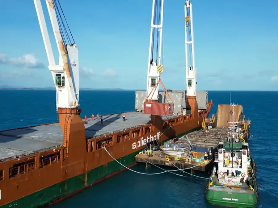 A cargo barge with deck cranes moored offshore in the Torres Strait, used to move recovered material off the islands.
