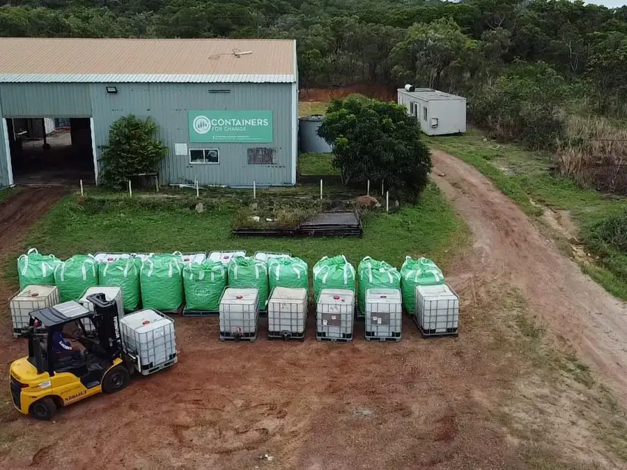 Aerial view of the Crystal Ailan depot on Badu Island: a shed signed Containers for Change, with a forklift moving pallets of filled green collection bags and water tanks.