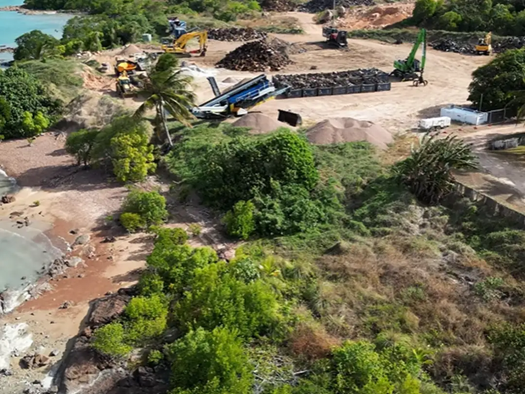 Aerial view of coastal site works in the Torres Strait, with earthmoving plant clearing and stabilising ground near the shoreline.