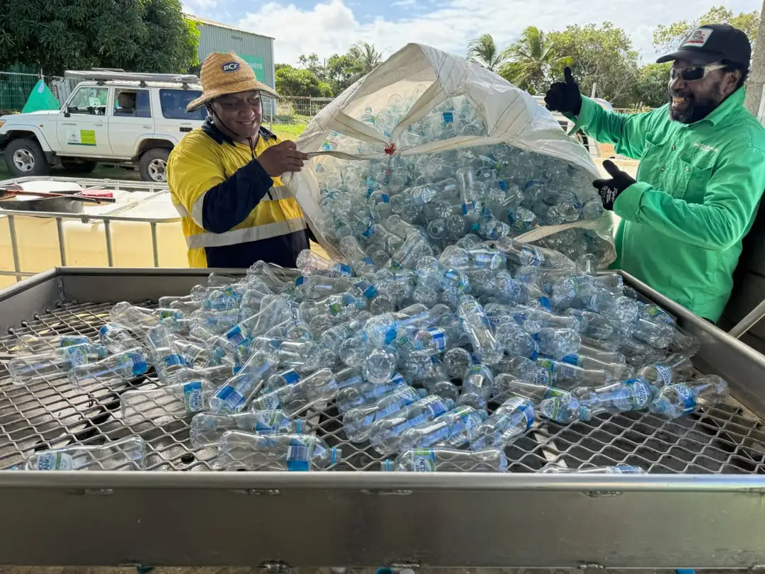 Two Crystal Ailan workers tipping a load of collected plastic drink bottles into a sorting cage on Badu Island.